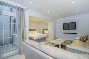 A modern hotel room with a large window, a sofa, a bed, a TV, and a mirror.