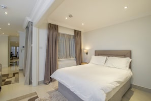 A modern bedroom with a large bed, a nightstand, and a window with curtains.
