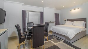 Une chambre d’hôtel comprenant un lit, un bureau avec une chaise, une télévision et une fenêtre avec des rideaux.