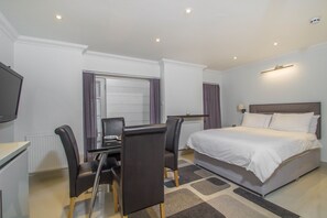 A hotel room with a bed, a desk with a chair, a television, and a window with curtains. - Spacious apartment for 4 (London)