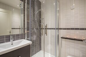 A modern bathroom with a glass-enclosed shower, a white sink, and a mirror. - Spacious apartment for 4 (London)