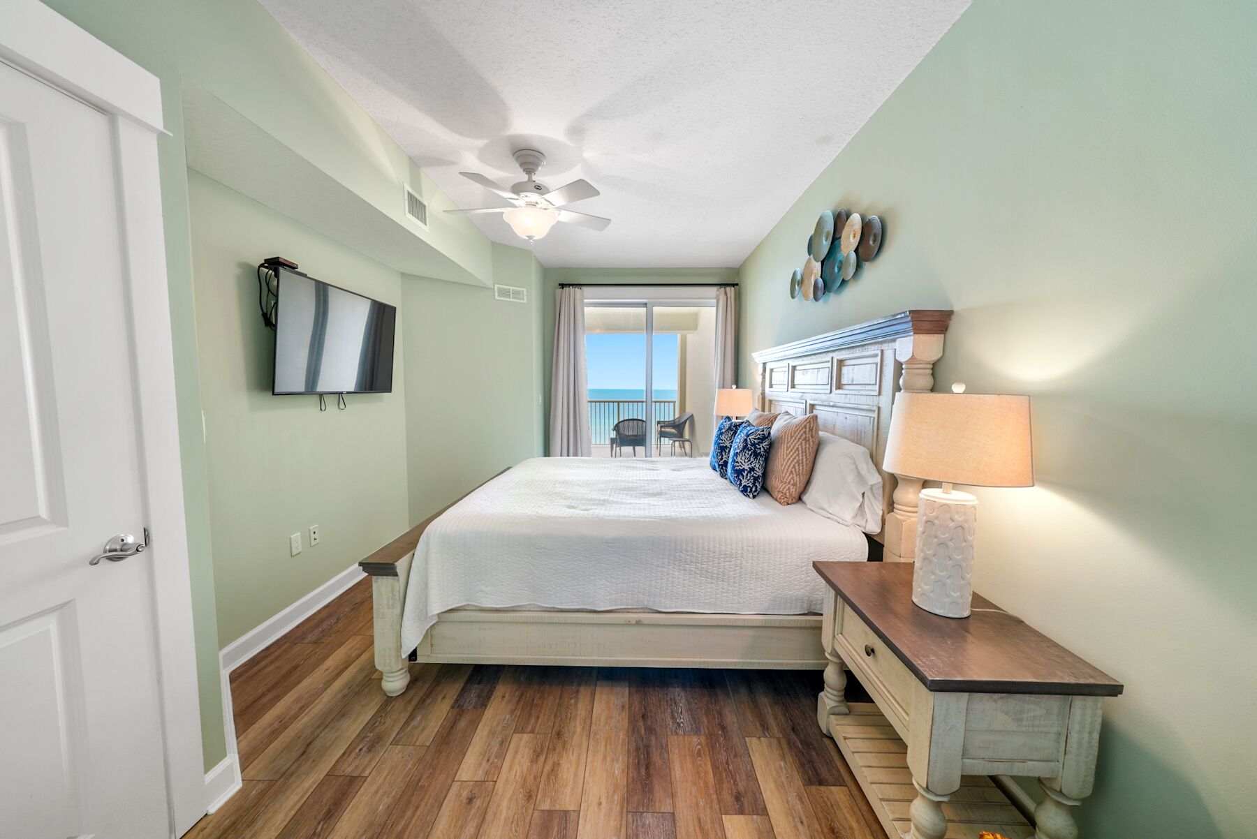A hotel room with a bed, a nightstand, a TV, and a view of the ocean.