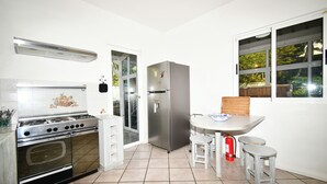 A kitchen with a gas stove, oven, stainless steel refrigerator, and a dining area with stools. - The Bay Villa 10 minutes by boat from Ile aux Cerfs (trou d'eau douce)