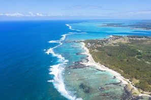 Vue aérienne d’une zone côtière avec une longue étendue de plage, des eaux d’un bleu limpide et une végétation luxuriante environnante.