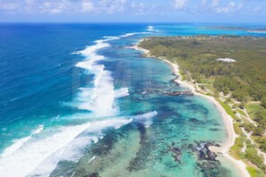 Luftaufnahme einer Küstenlandschaft mit klarem türkisblauem Wasser, einem Sandstrand und dichtem Grün.