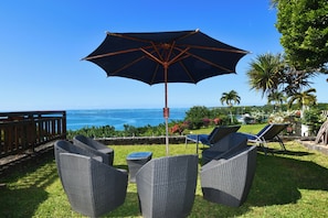Eine Terrasse mit Korbmöbeln, einem großen Sonnenschirm und Blick auf das Meer.