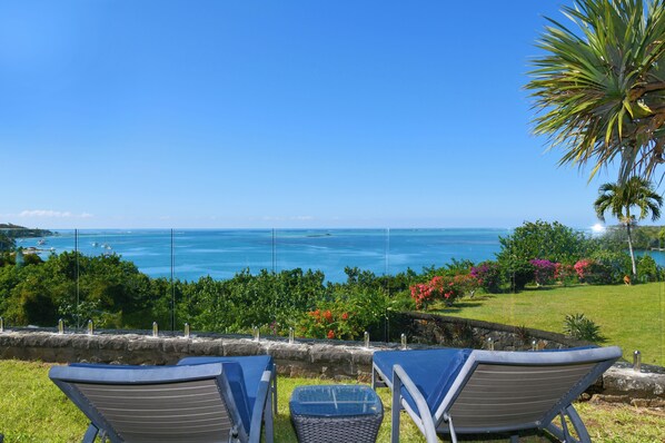 A view of the ocean with a clear sky, two lounge chairs, and a stone wall.