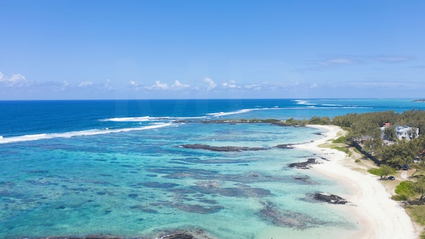 A coastal view with clear turquoise waters, a sandy beach, and a building with a red roof. - The Bay Villa 10 minutes by boat from Ile aux Cerfs (trou d'eau douce)