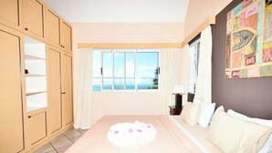 A bedroom with a bed, a window with a view of the sea, a wardrobe, and a wall with a decorative piece. - The Bay Villa 10 minutes by boat from Ile aux Cerfs (trou d'eau douce)