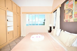 Ein Schlafzimmer mit Bett, einem Fenster mit Meerblick, einem Kleiderschrank und einer Wand mit einer Dekoration.
