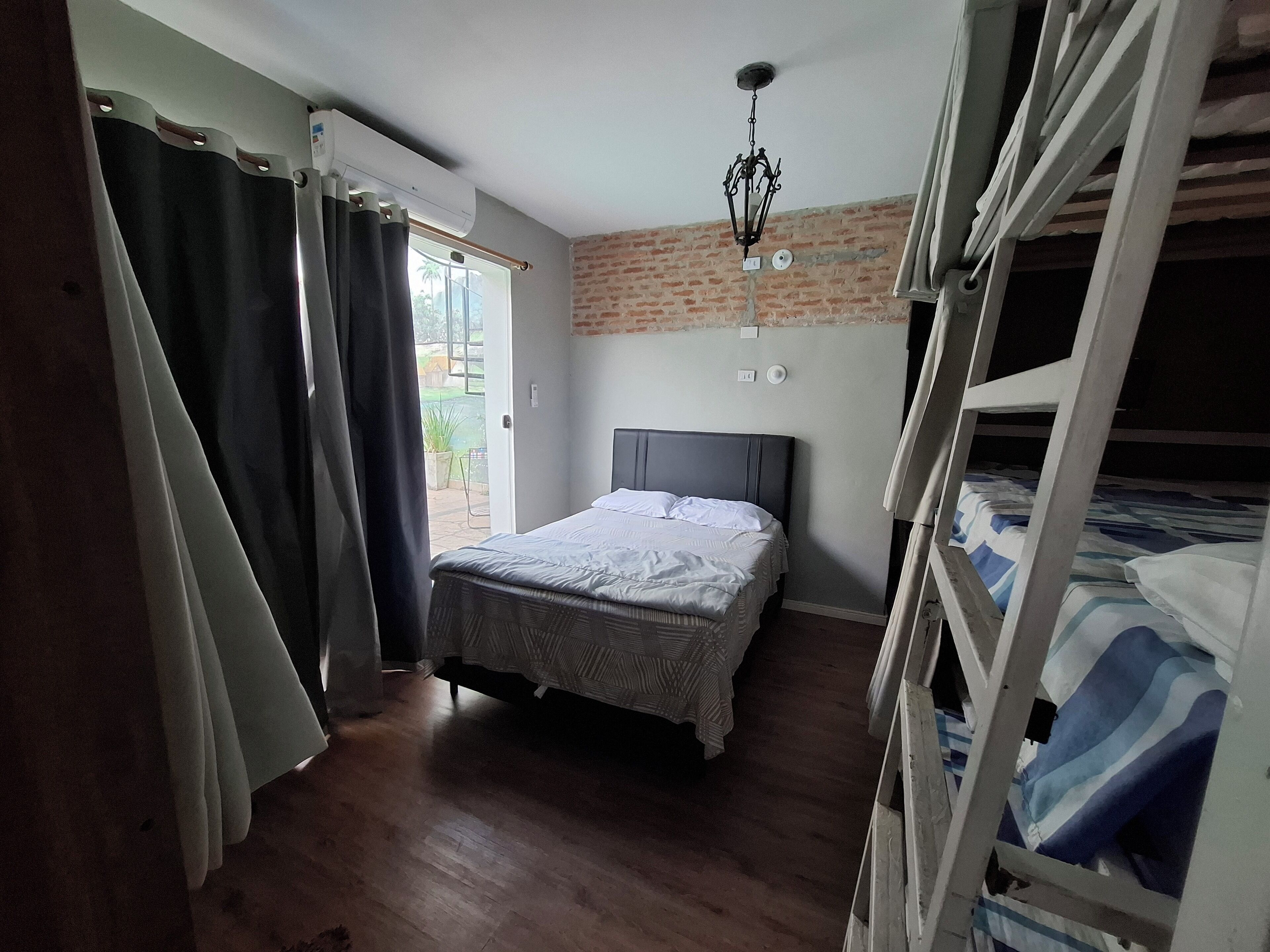 A bedroom with a bed, a window, a brick wall, and a bunk bed.