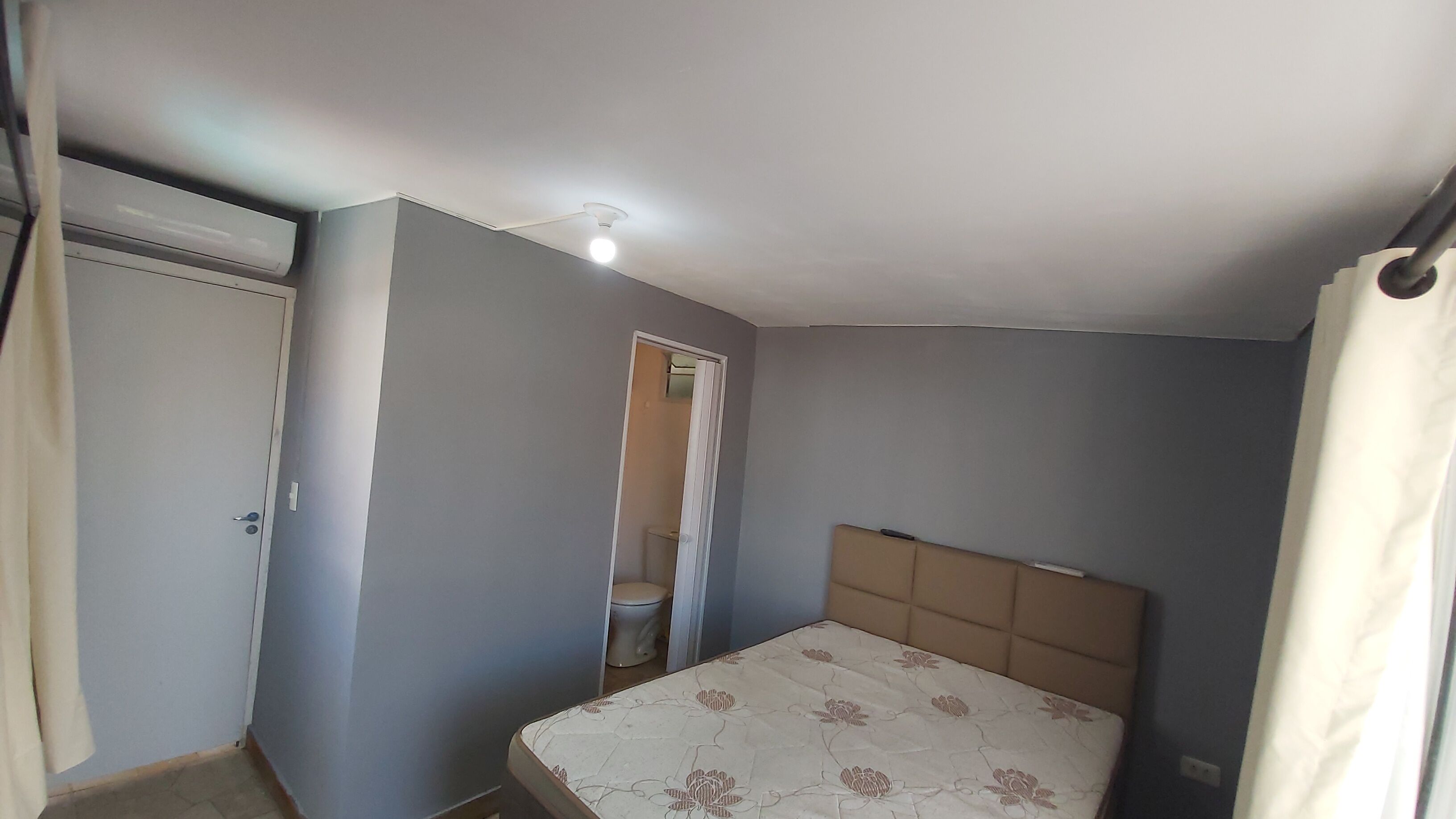 Um apartamento pequeno, de um único quarto, com uma cama, um vaso sanitário e uma porta.