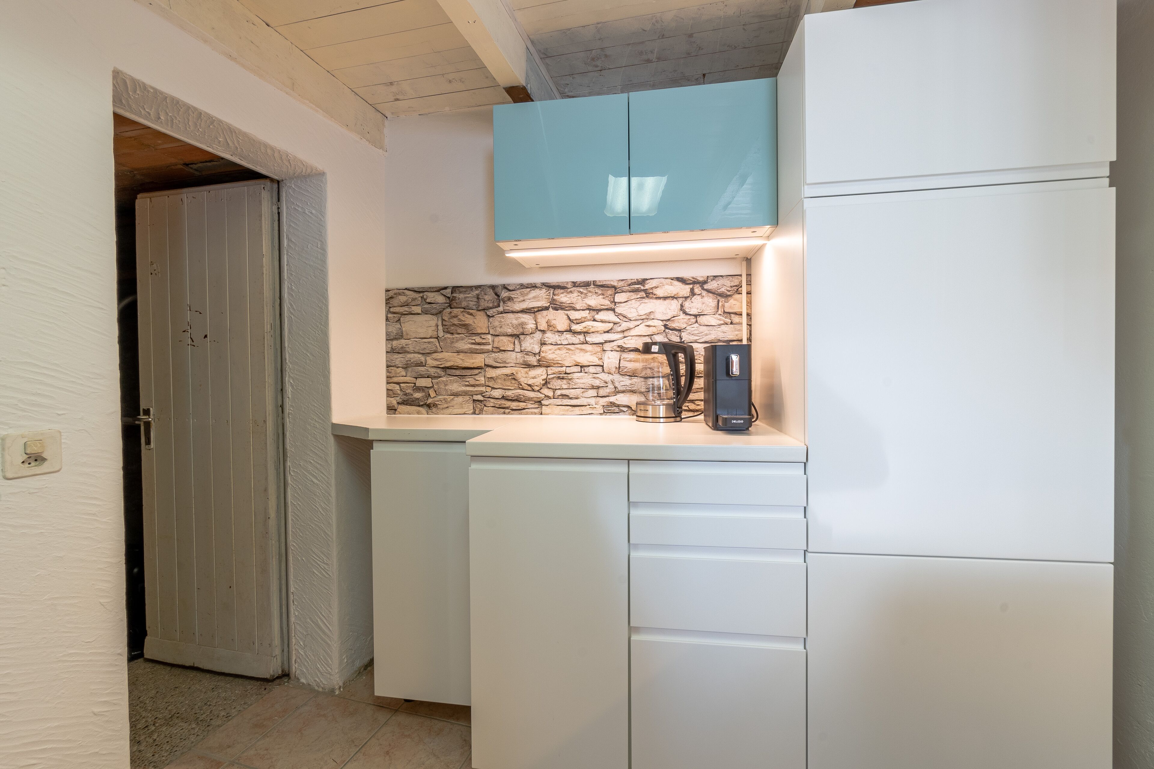 Una cocina compacta con armarios blancos, salpicadero de piedra y cafetera integrada.