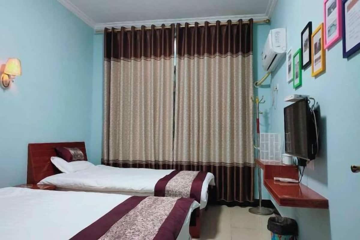 Une chambre d’hôtel avec deux lits, une télévision, une petite table et un climatiseur fixé au mur.