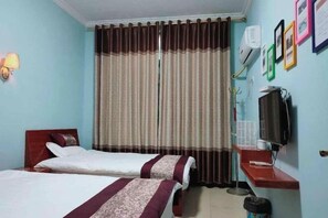 A hotel room with two beds, a TV, a small table, and a wall-mounted air conditioner.