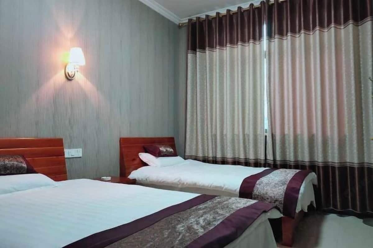 Une chambre d’hôtel avec deux lits, une lampe fixée au mur et une fenêtre avec des rideaux.