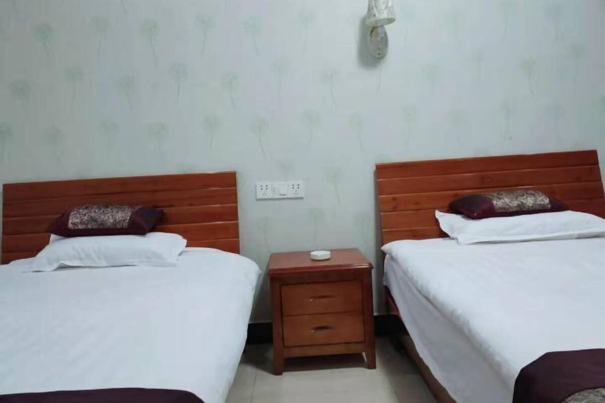 Une chambre avec deux lits, chacun doté d’une tête de lit en bois, d’une petite table de chevet et d’une prise électrique au mur.