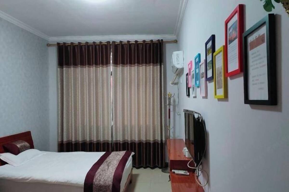 Une chambre d’hôtel avec un lit, des rideaux, une télévision et des tableaux encadrés au mur.