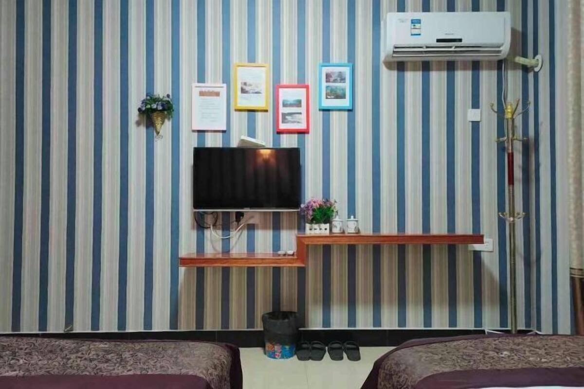 Une chambre d’hôtel avec un papier peint à rayures, un téléviseur fixé au mur, une petite étagère avec des objets décoratifs et deux lits.