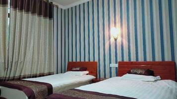 A hotel room with two beds, striped wallpaper, a wall-mounted light, and a window with curtains.
