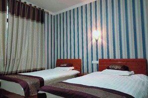 A hotel room with two beds, striped wallpaper, a wall-mounted light, and a window with curtains.