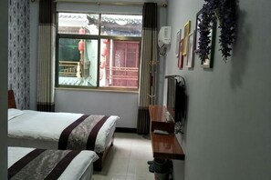 A hotel room with two beds, a wooden desk, a window with a view of a traditional building, and a wall-mounted air conditioner.