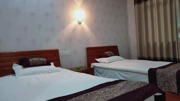 A hotel room with two beds, a wall-mounted light, a curtain, and a nightstand with a green object. - Tongle Inn (Wuyuan)