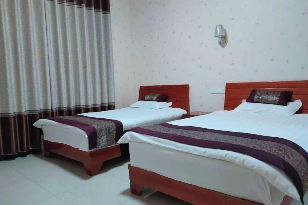 Une chambre d’hôtel avec deux lits simples, un rideau, une lampe fixée au mur et un sol carrelé.