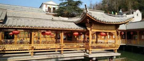 A traditional Chinese building with a wooden structure and red lanterns, situated over water.