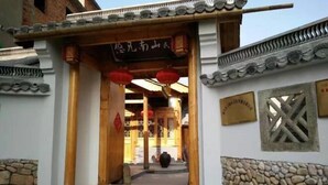 A traditional building entrance with a wooden door, red lanterns, and a stone wall. - Youjian Nanshan Hotel (Xinchang)