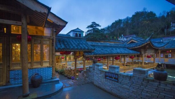 A traditional courtyard with wooden buildings, stone walls, and a small bridge. - Youjian Nanshan Hotel (Xinchang)