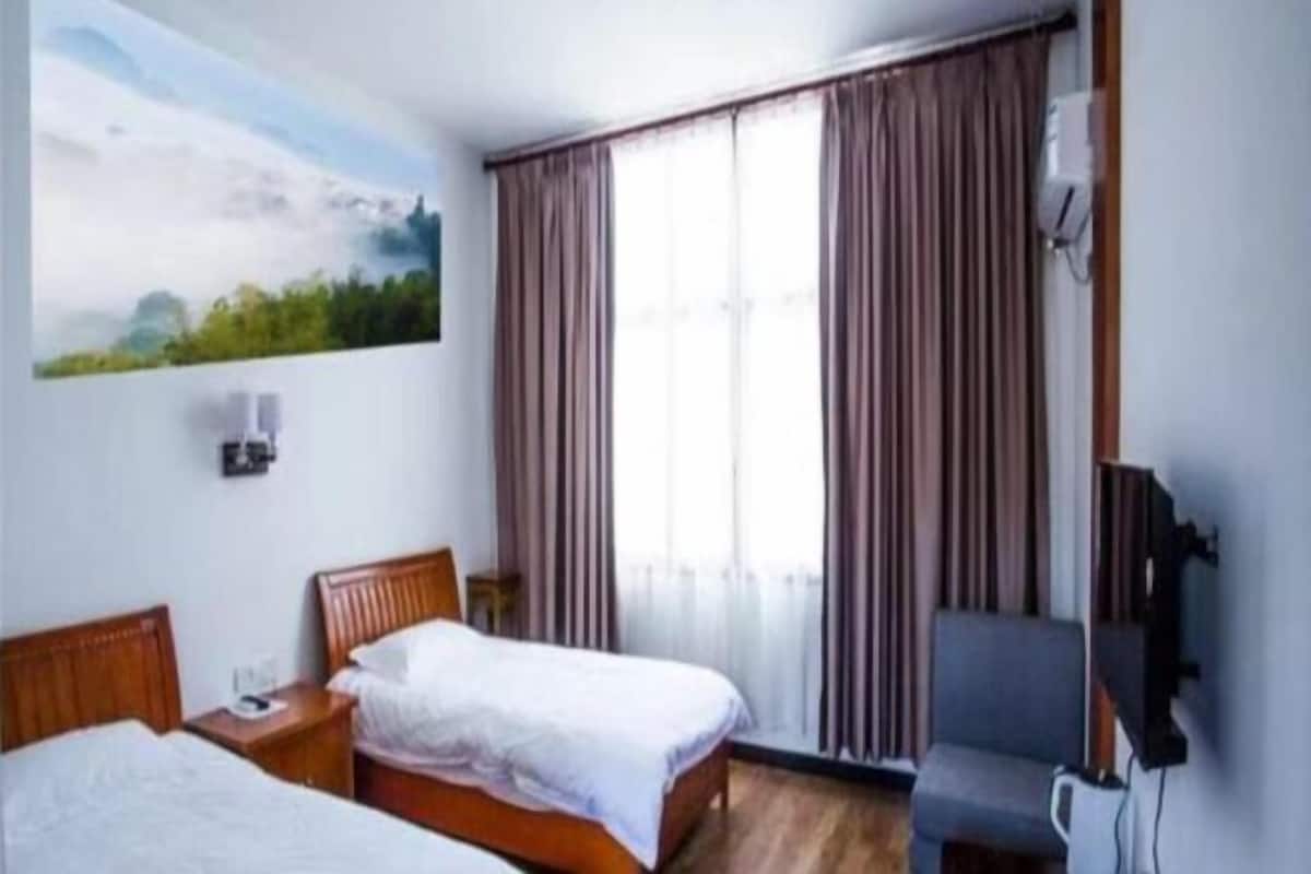 A hotel room with two beds, a TV, a chair, and a large window with curtains.
