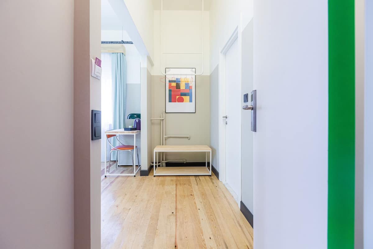A narrow hallway with a wooden floor, a bench, and a framed artwork on the wall.