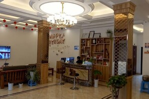 Un área de recepción con una araña, un televisor, un mostrador de recepción y una pared con un letrero.