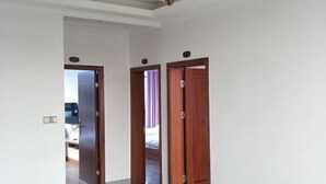 A hallway with two wooden doors, a ceiling light fixture, and a visible room with a bed and curtains. - Junda Hotel (Anji)