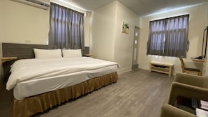 Habitación de hotel con una cama grande, un escritorio, una silla y una mesita pequeña. Tiene una ventana con cortinas, un aire acondicionado y una puerta.