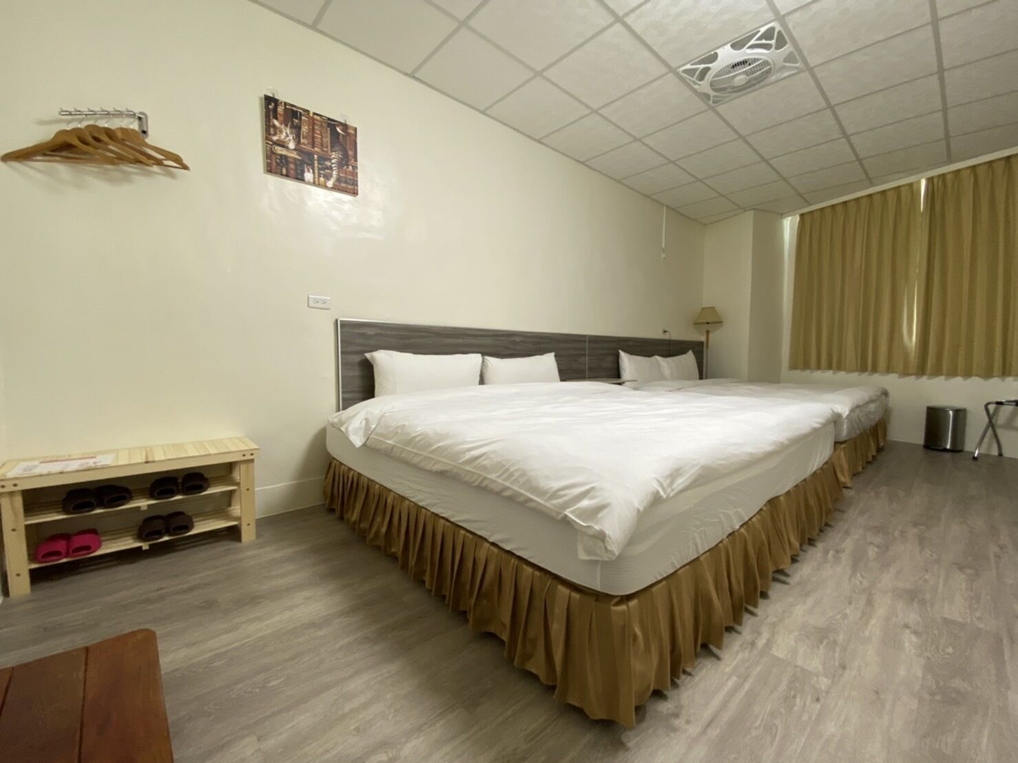 A hotel room with a large bed, a wooden shoe rack, a small table, and a window with curtains.