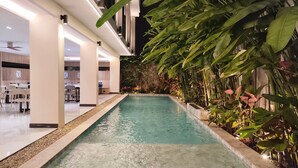 A swimming pool with a pebble-lined edge, surrounded by lush tropical plants. - Hi Chiangmai Hotel (Chiang Mai)