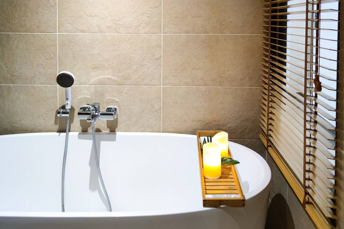 A modern bathroom with a freestanding bathtub, a showerhead, and a wooden shelf with a candle.