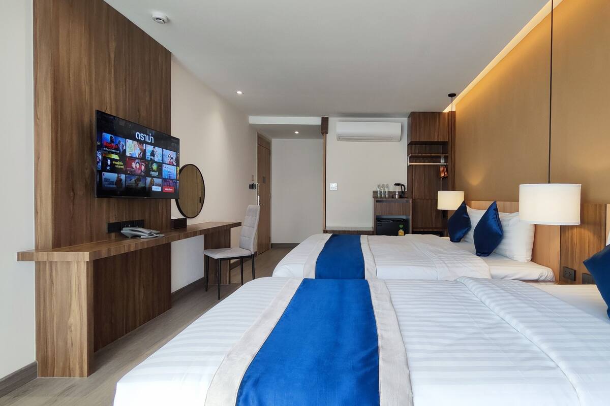 A hotel room with two beds, a TV on the wall, a desk with a chair, and a minibar.