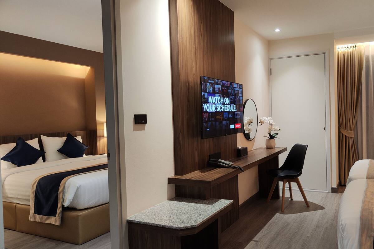 A hotel room with a bed, a desk with a computer, a TV, and a chair.