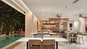 A modern dining area with a pool view, featuring a long table with chairs, a bar area, and ceiling fans. - Hi Chiangmai Hotel (Chiang Mai)