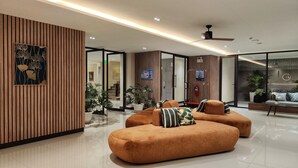 A modern lobby with a wooden panel wall, a ceiling fan, and a seating area with orange sofas and decorative pillows. - Hi Chiangmai Hotel (Chiang Mai)