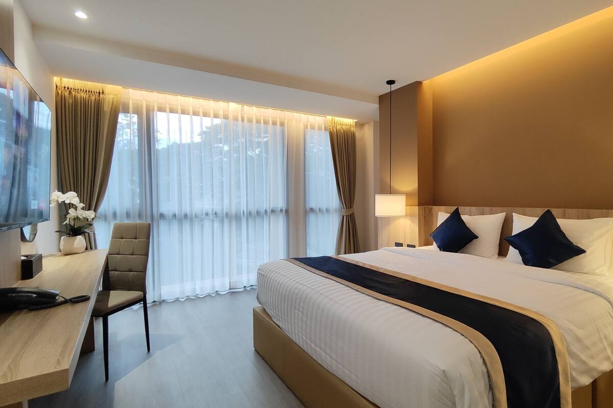 A modern hotel room with a large bed, bedside lamps, a desk with a telephone, and a TV.