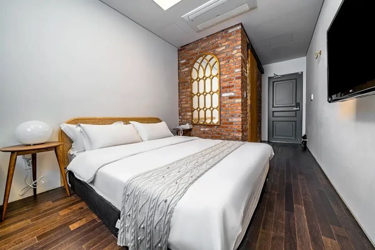 Una camera da letto con un letto, un comodino, una TV a parete e una parete decorata con mattoni.