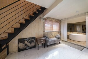 Un interior moderno con una escalera de madera, un sofá, un ventanal con persianas y un baño con bañera.