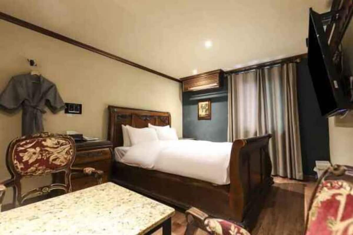 Una camera d'albergo con un letto, una scrivania, una sedia, una televisione e una finestra con tende.
