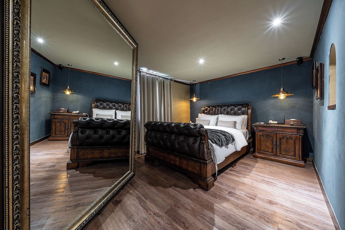 Una camera da letto con un grande specchio, un letto con testiera, un comodino e una cassettiera.