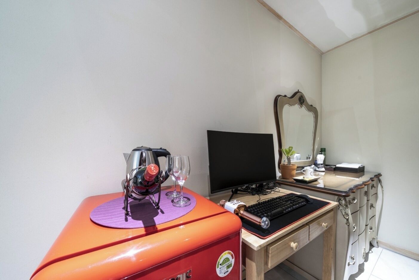 A compact room with a desk, a computer, a mirror, and a small potted plant.