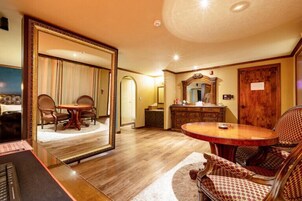 Una habitación espaciosa con un espejo grande, una mesa redonda de madera y un área de descanso con sillas estampadas.